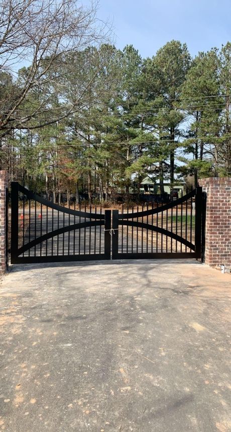 A black gate is sitting in the middle of a driveway next to a brick wall.