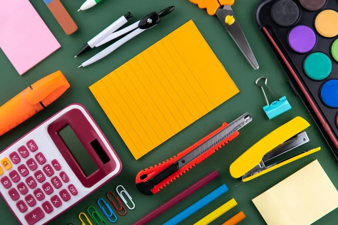 A variety of school supplies are laid out on a green table.