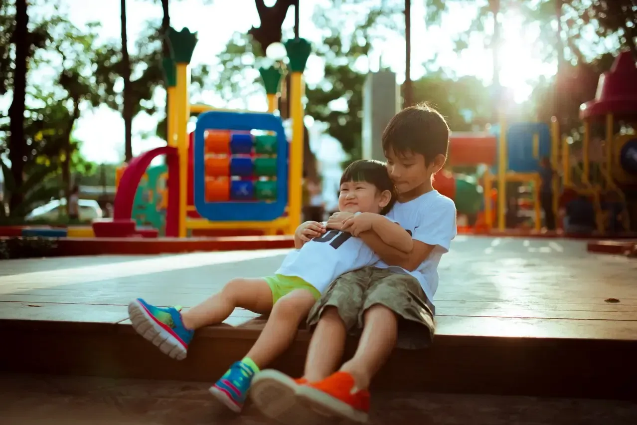 A boy and a girl are sitting next to each other in front of a playground.