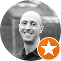 A bald man is smiling in a black and white photo with an orange star.