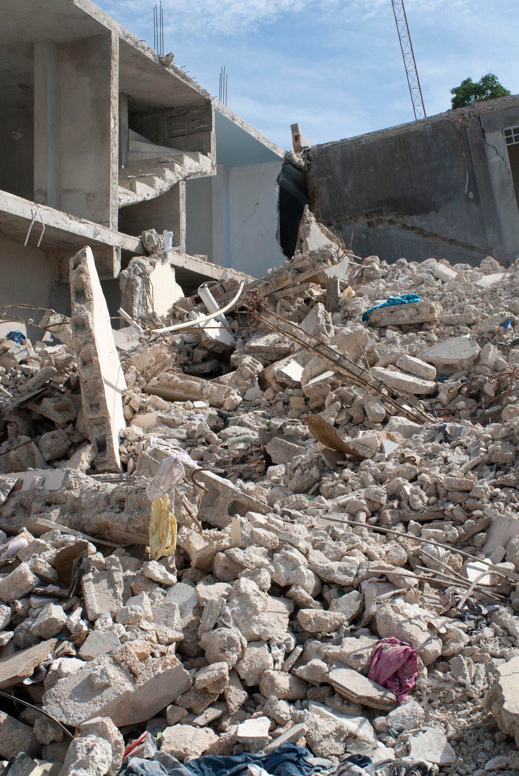 Debris pile in front of a partially destroyed building under a blue sky.