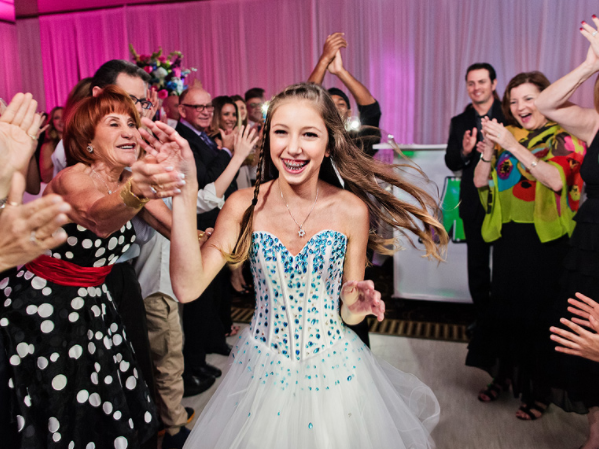 a girl in a white dress is dancing in front of a crowd of people at her bat mitzvah.