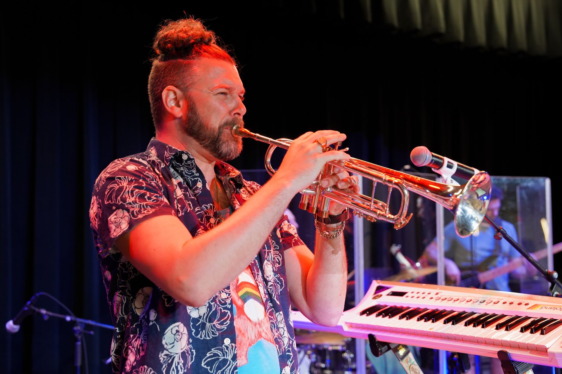 A man is playing a trumpet on a stage in front of a keyboard.