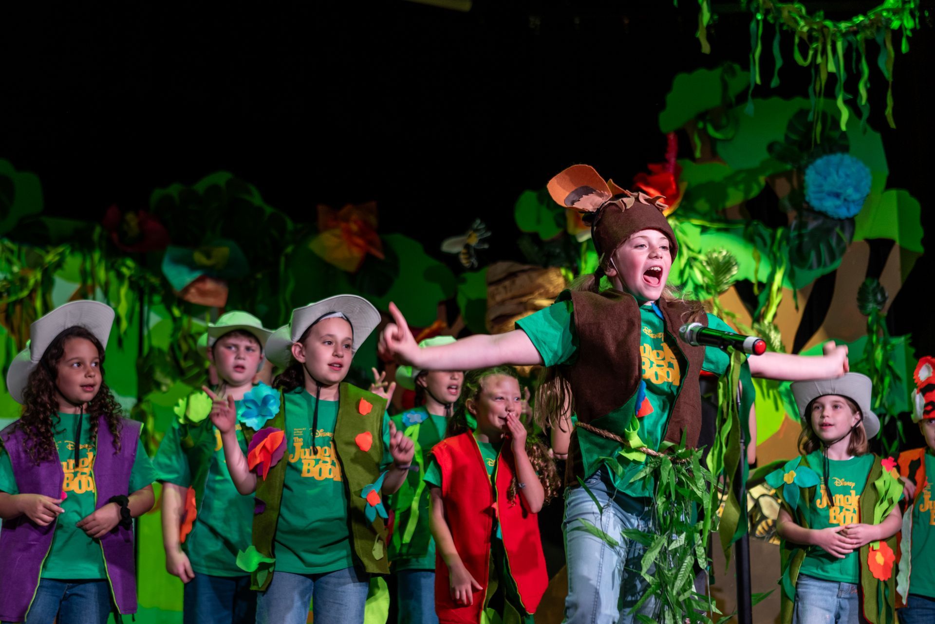 A group of children are singing into microphones on a stage.