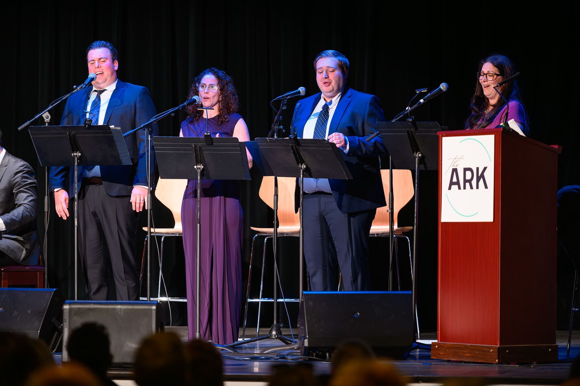 A group of people are singing into microphones on a stage.