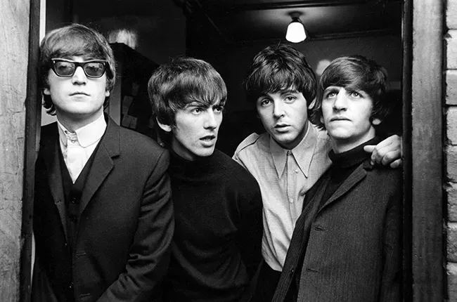 The Beatles, four men, huddled close together in a doorway. Black and white photo.