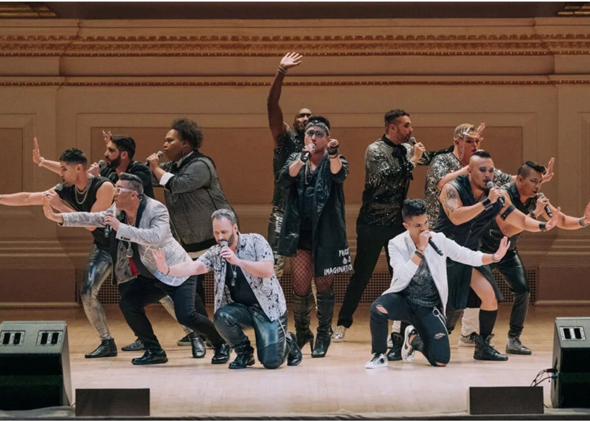 A large choir in black attire, led by a conductor in a suit, on a stage with a dark backdrop.