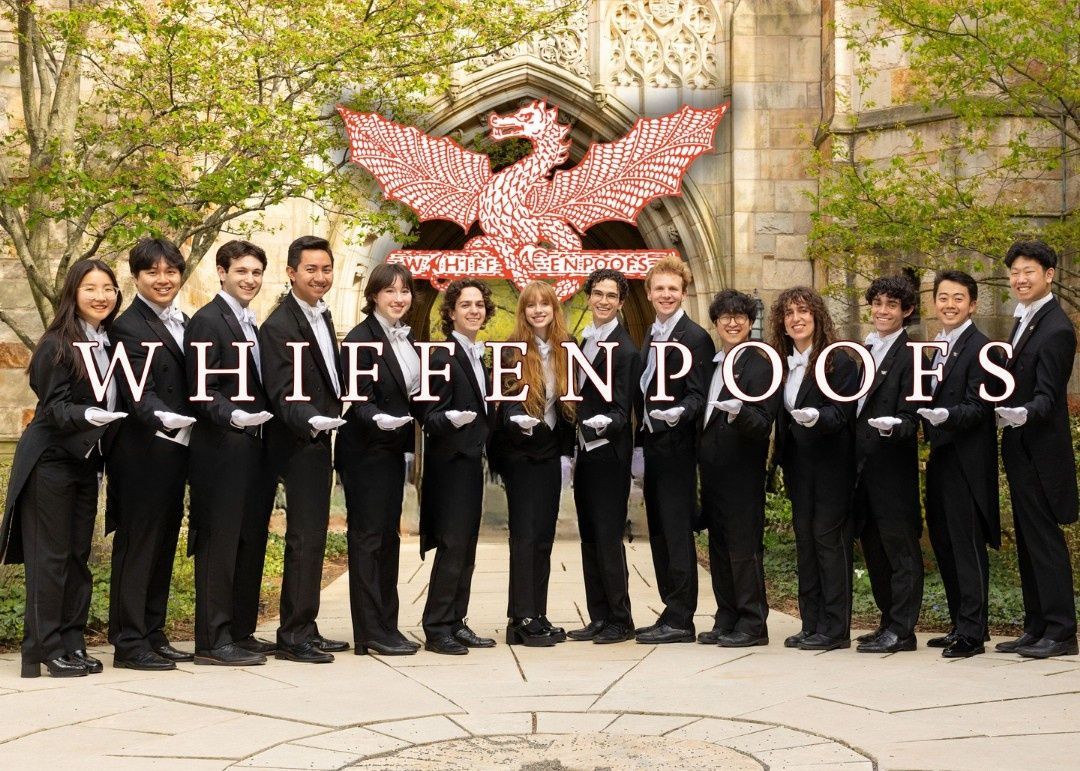 The Whiffenpoofs, a cappella group, in black tuxedos, posed in front of a building with a crest logo.