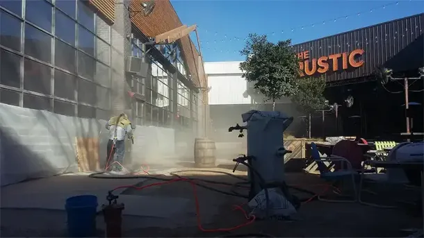 A worker stands on a stone lion statue to clean the exterior stone wall of a building marked with ΣΑΕ and the number 2414.
