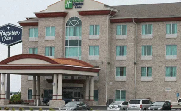 Hotel building with sign, awning, and parked cars; light brick exterior, Hampton Inn sign in front.