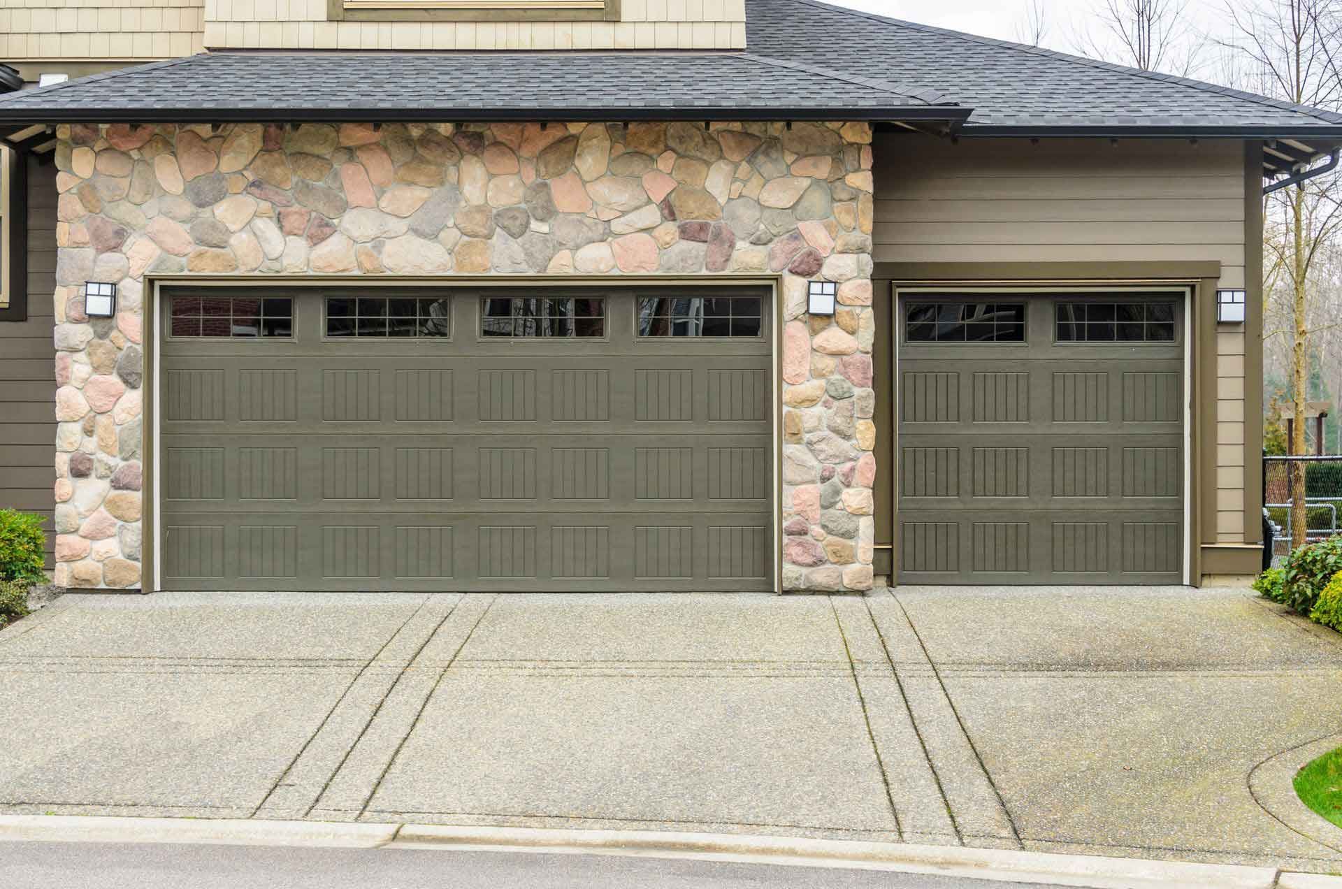 Two-car garage with two olive green doors; stone facade; concrete driveway.