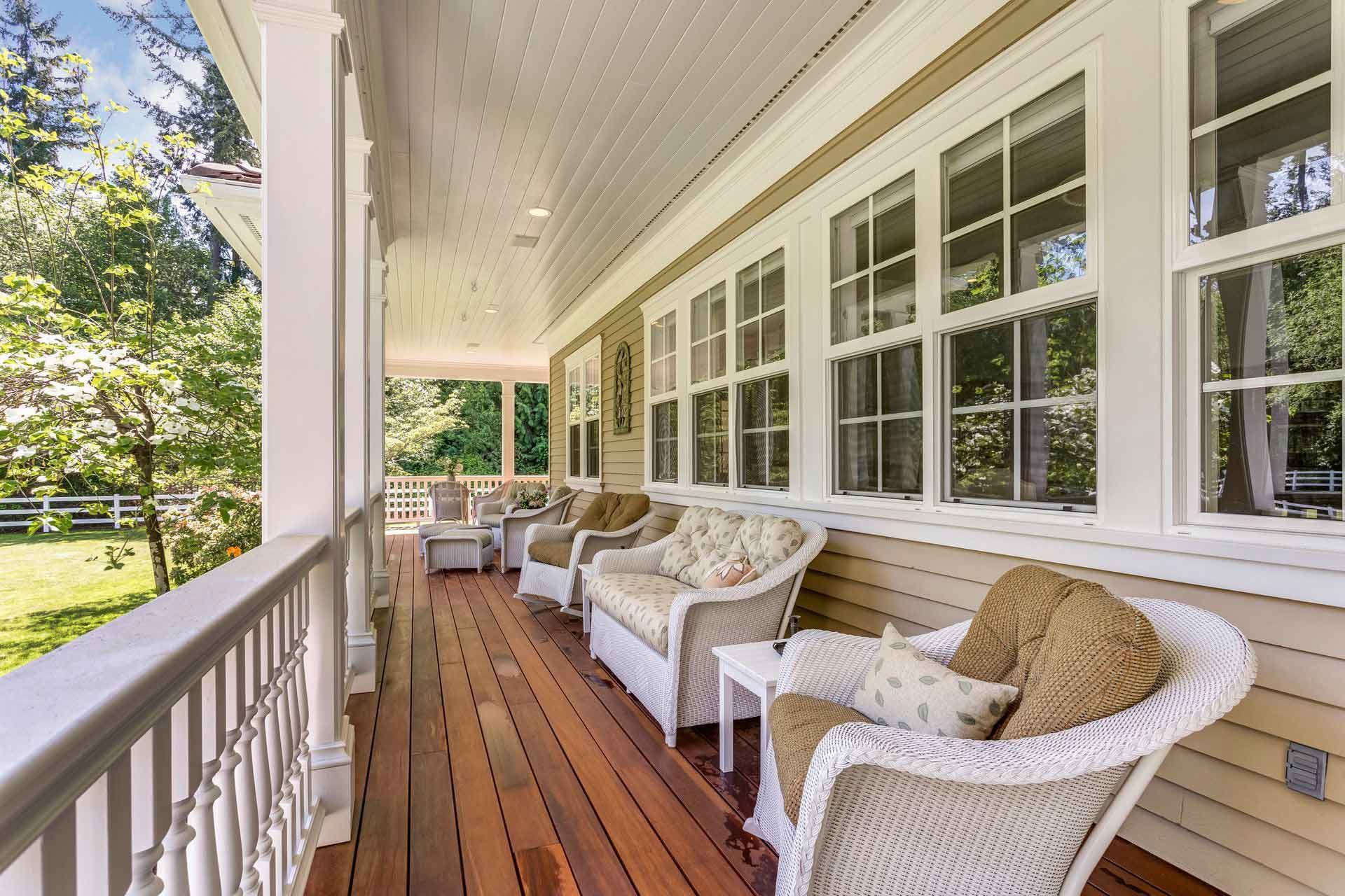 Long covered porch with white wicker chairs, wood flooring, and large windows.