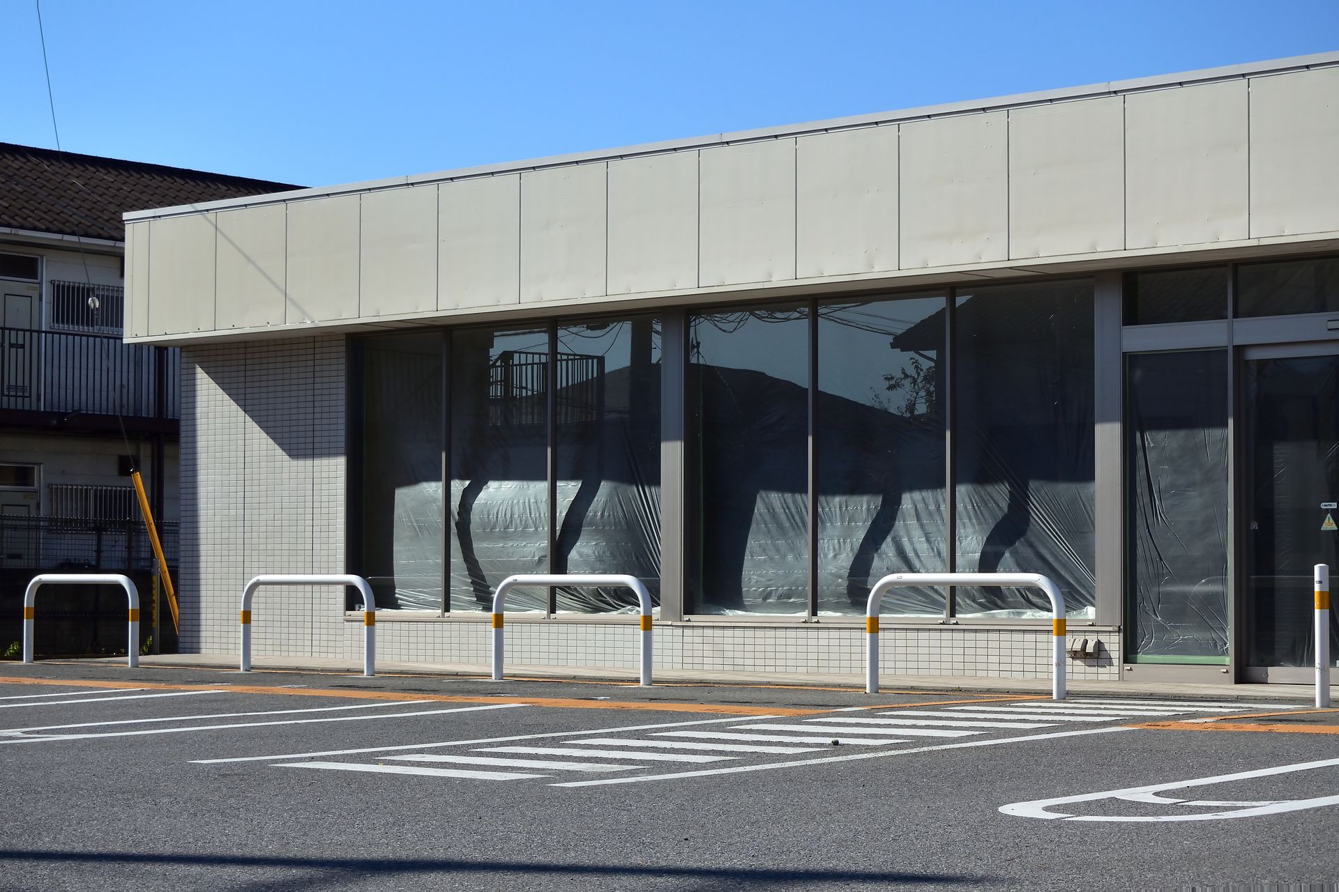 Exterior of a building with large windows reflecting surroundings. Parking area in front with bike racks.