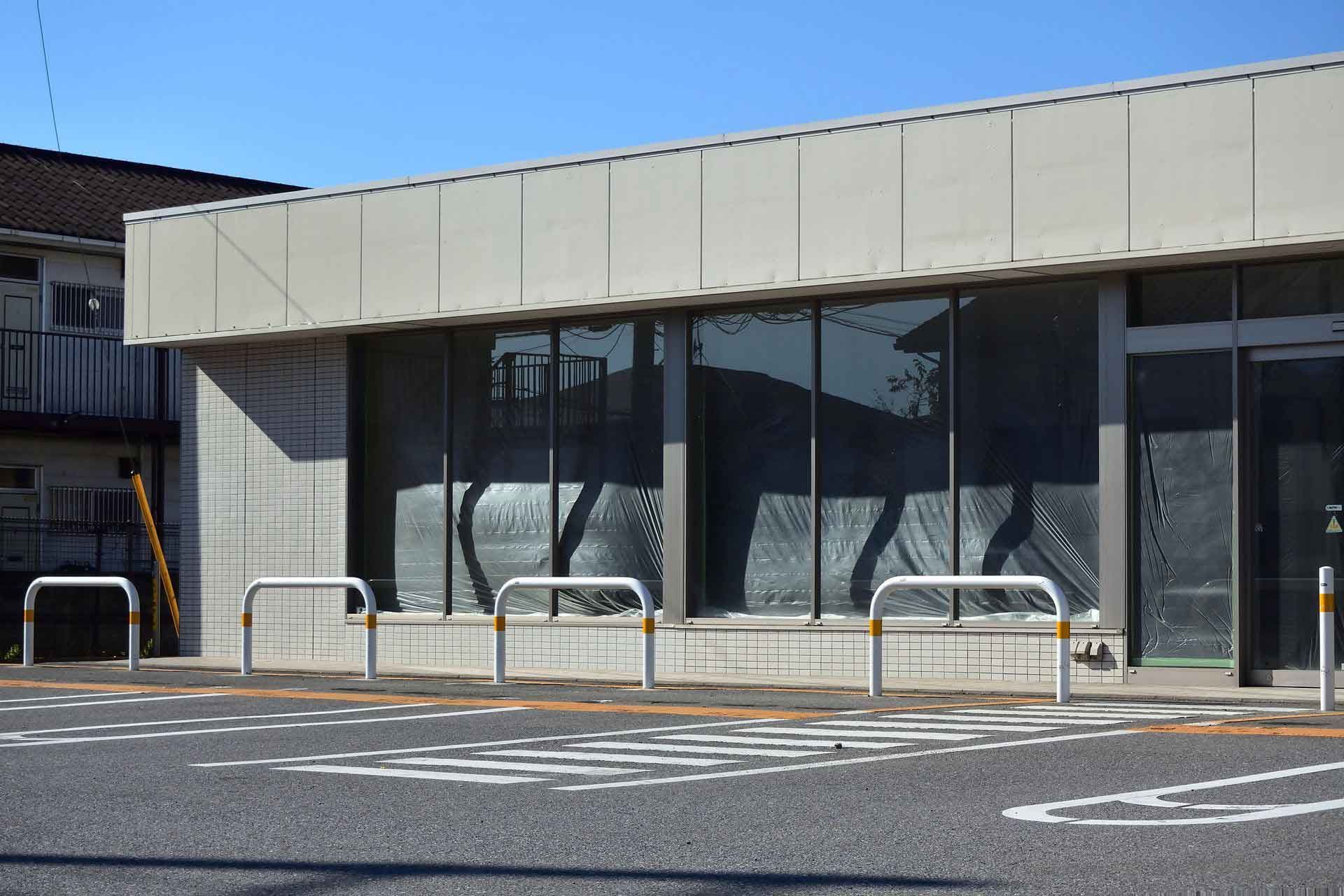 Exterior of a building with large windows reflecting surroundings. Parking area in front with bike racks.
