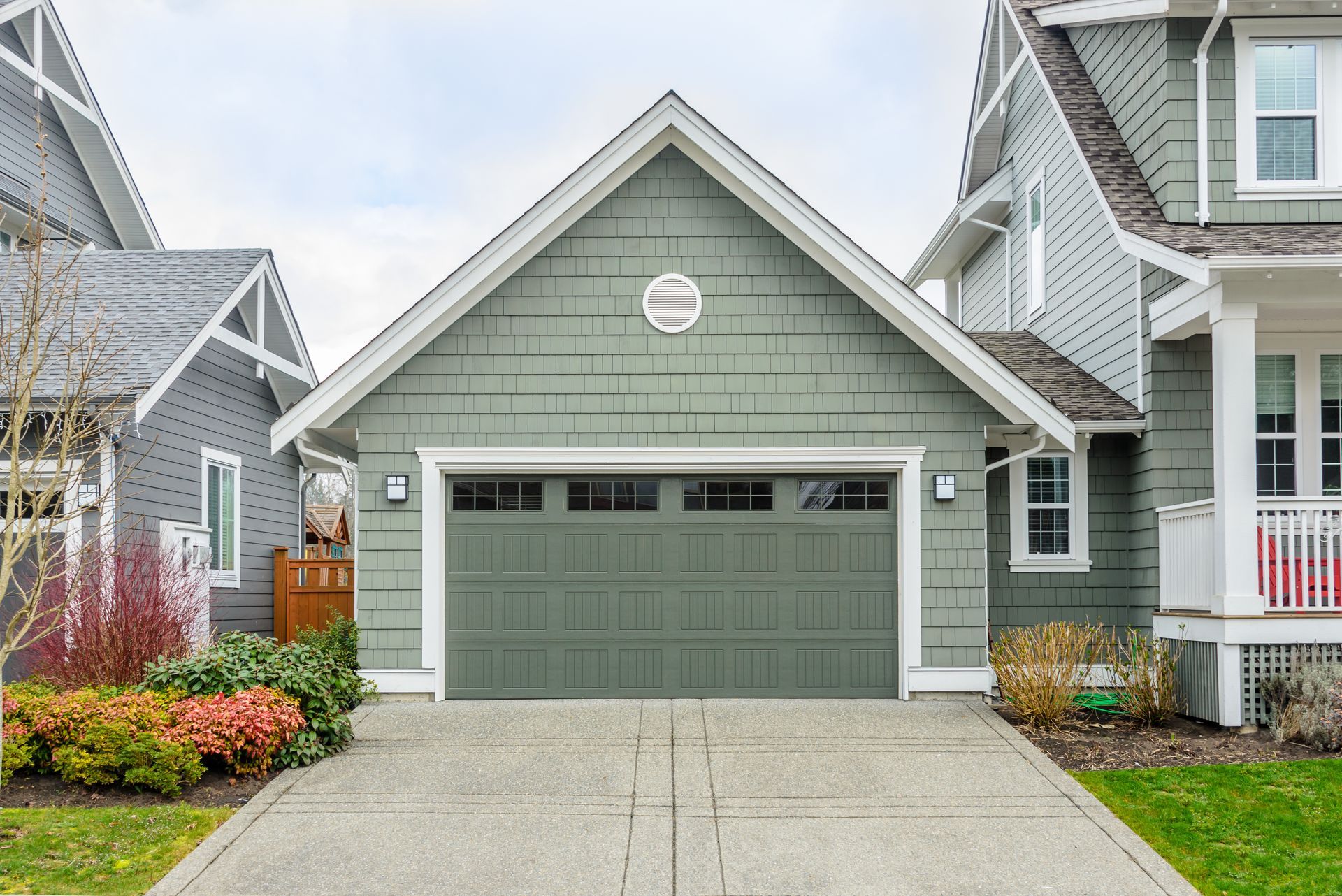 Green garage with driveway between two houses, overcast sky.