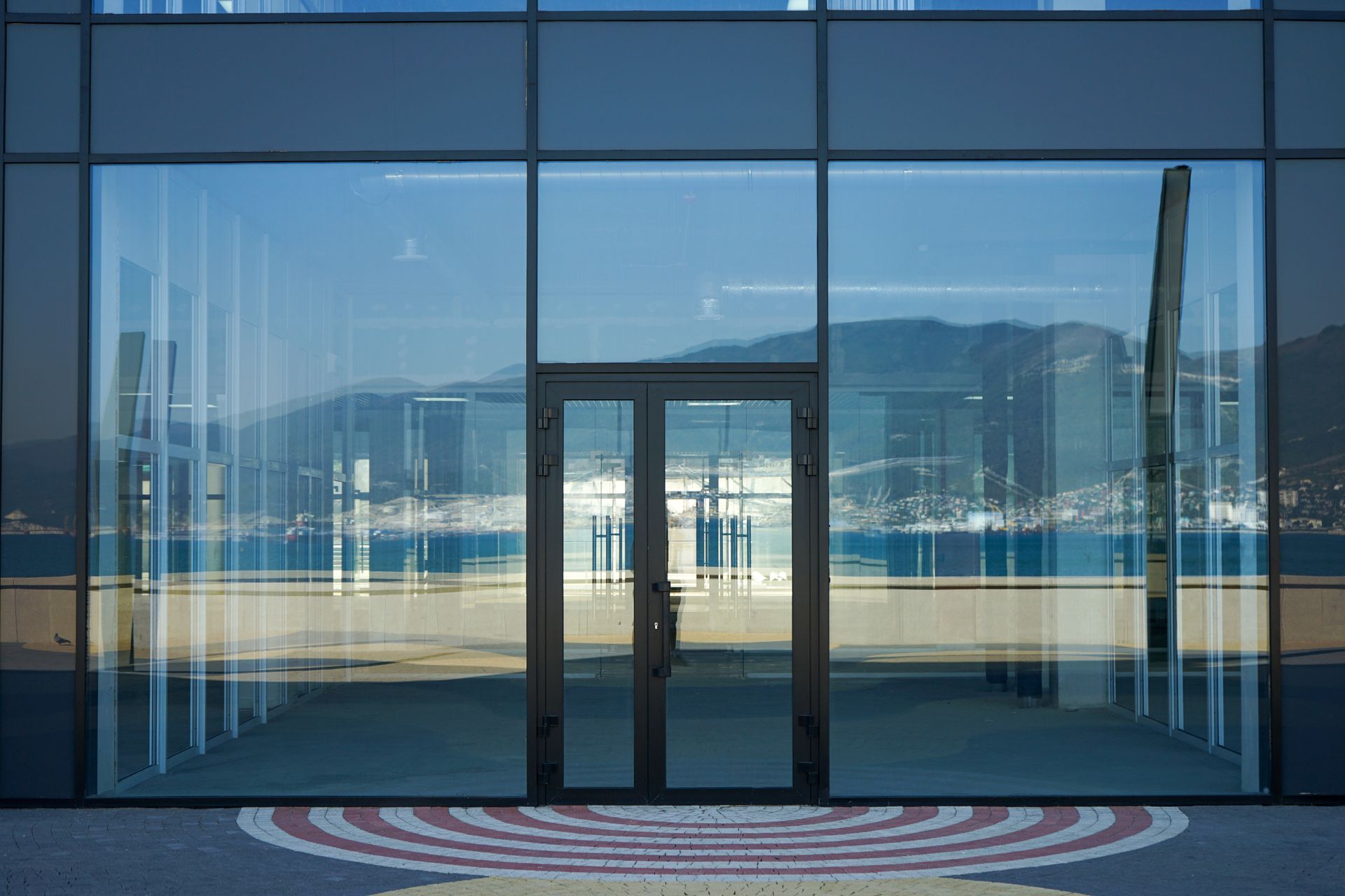 Glass building entrance with mirrored reflection of mountains and water.