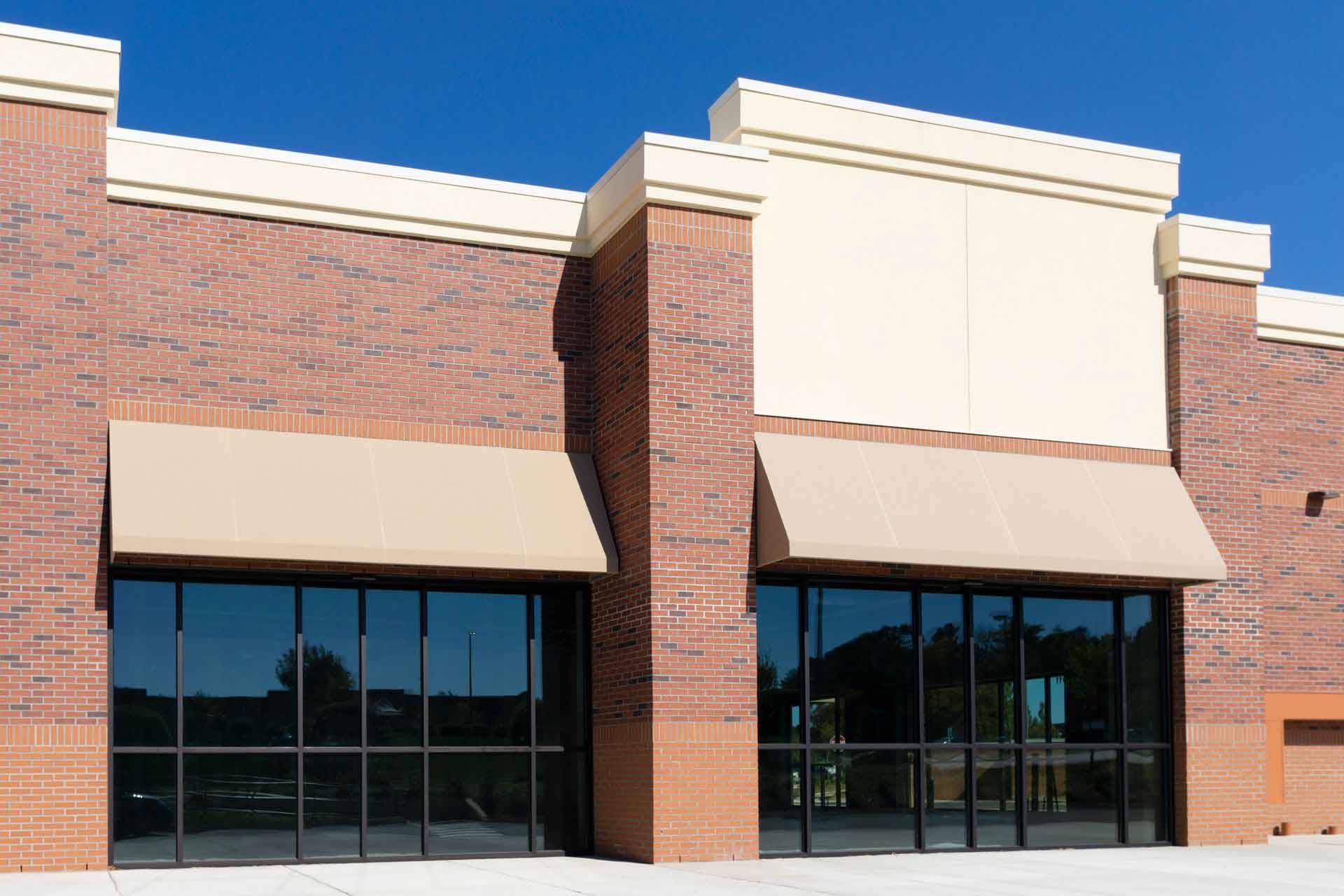 Commercial building with brick facade, large windows, tan awnings, and a clear blue sky. Commercial building with brick facade, large windows, tan awnings, and a clear blue sky.