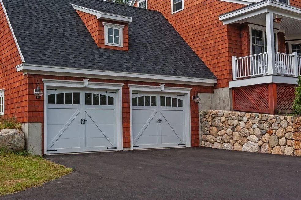 Two white garage doors on a red-sided house with a dark roof and a porch.
