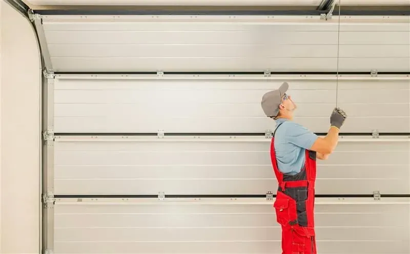 Person in red overalls inspecting a partially open garage door, looking up at the mechanism.