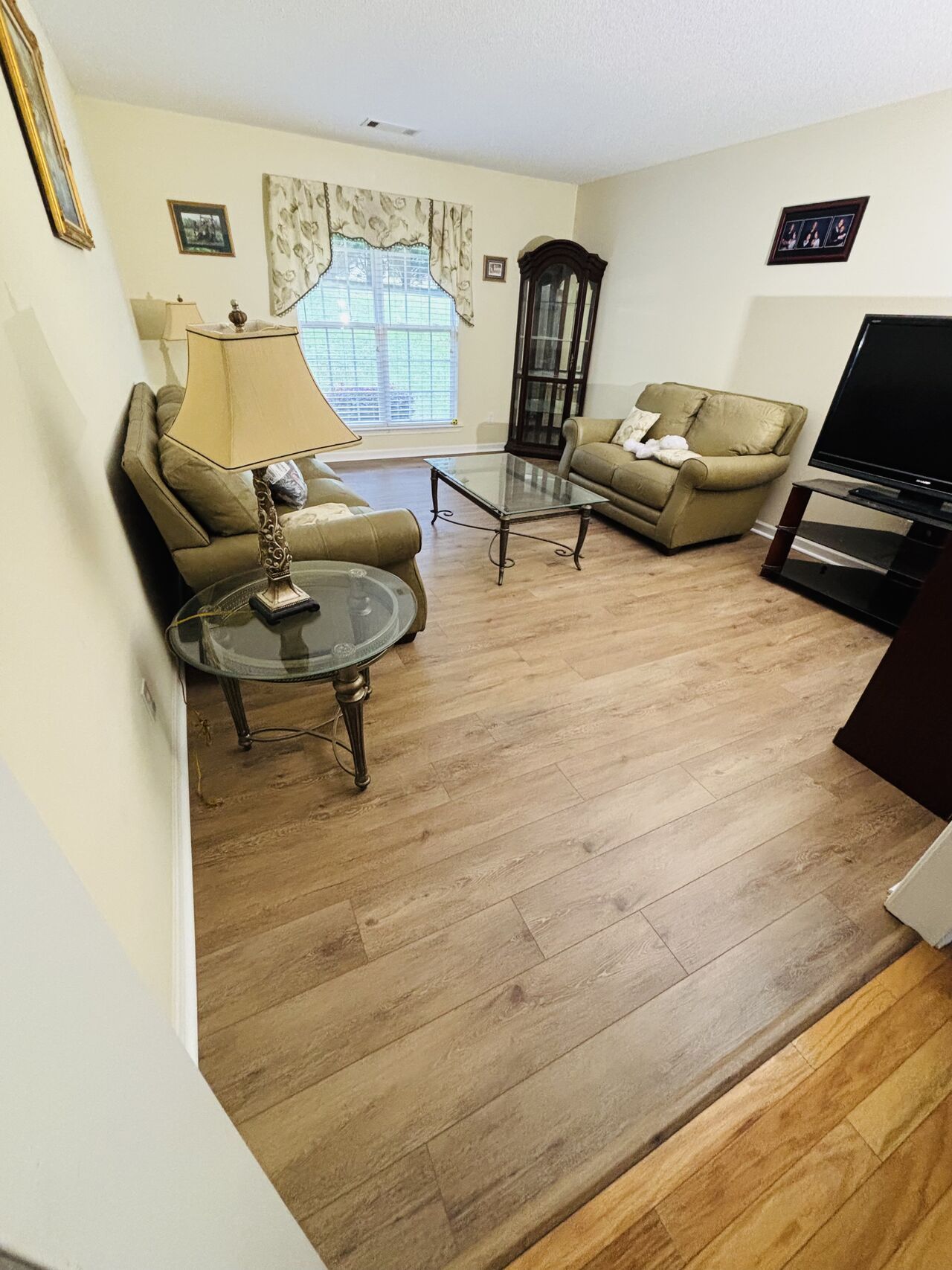 Living room with light wood floors, two beige sofas, glass coffee table, and a grandfather clock.