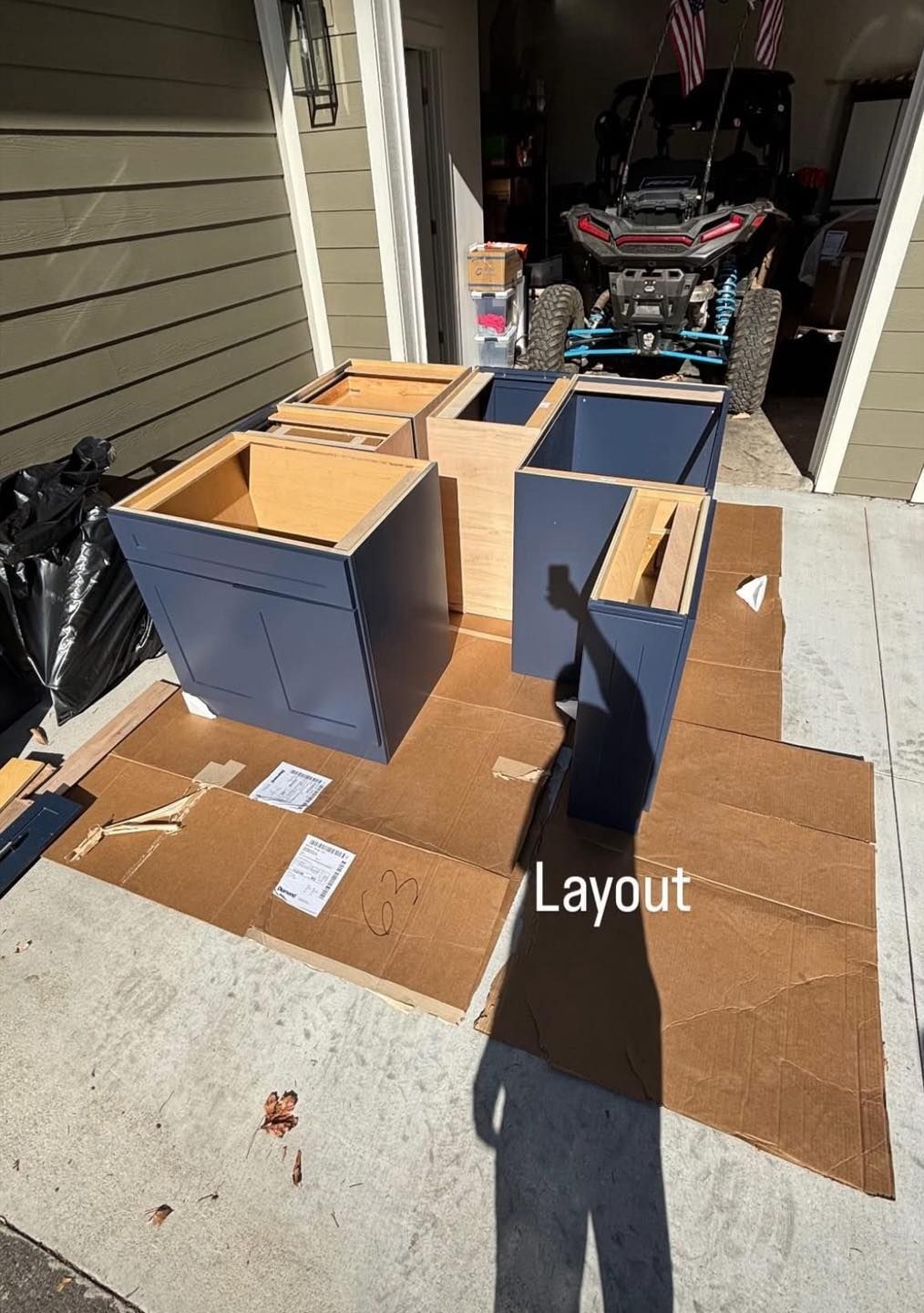 Assembled blue cabinets arranged on cardboard in a driveway. A side-by-side vehicle is in the background.