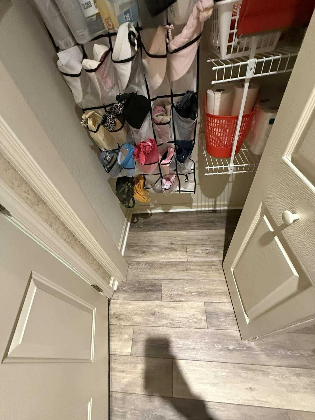 Closet with shoes in a hanging organizer and shelf with supplies. Gray floor and white doors.