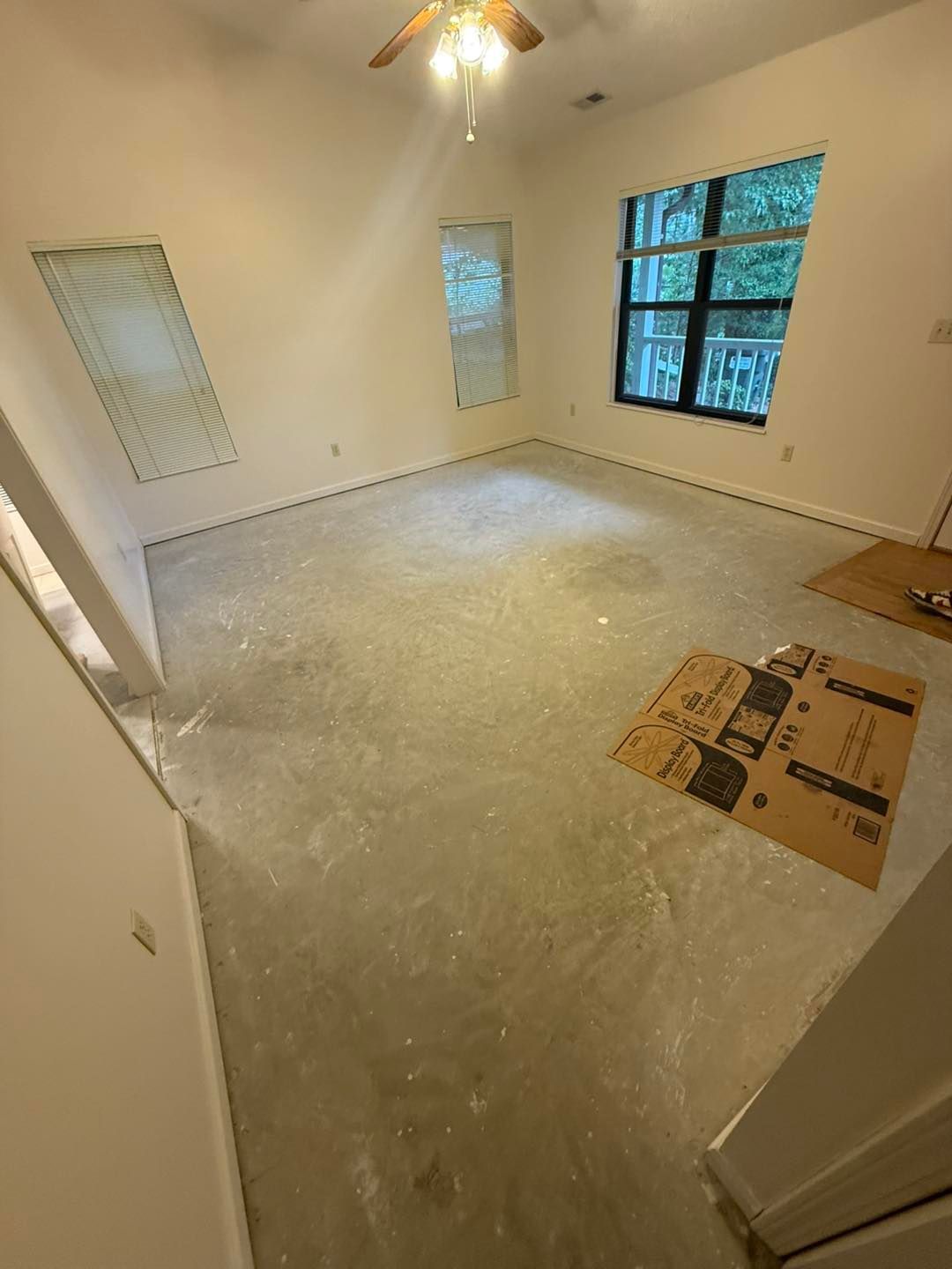 Empty room with concrete floor, three windows, and a ceiling fan.