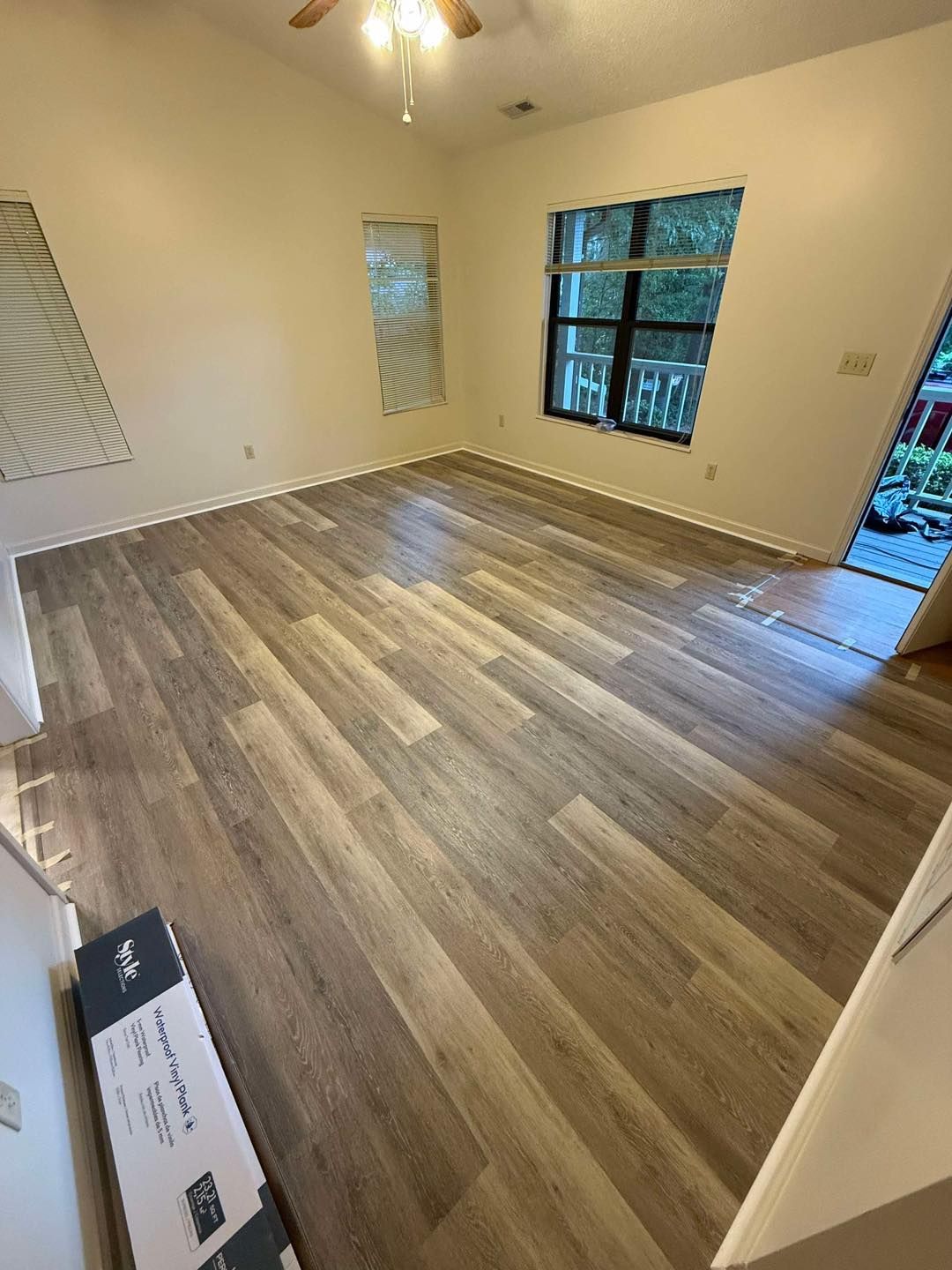 Empty room with newly installed wood-look flooring, beige walls, and a window.