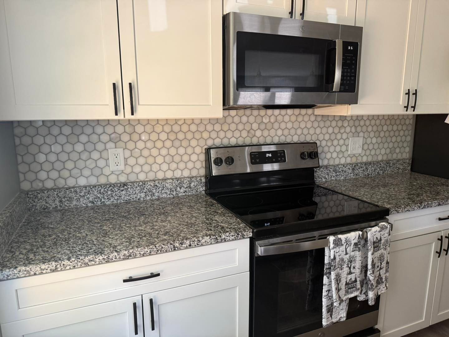 Kitchen with white cabinets, gray countertops, and a stainless steel oven and microwave. Penny tile backsplash.