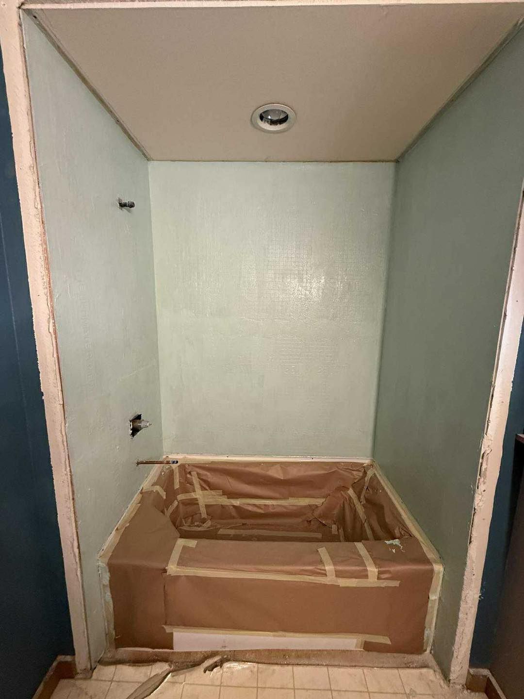 Empty shower stall with protective covering, light green walls, a recessed light, and surrounding blue walls.