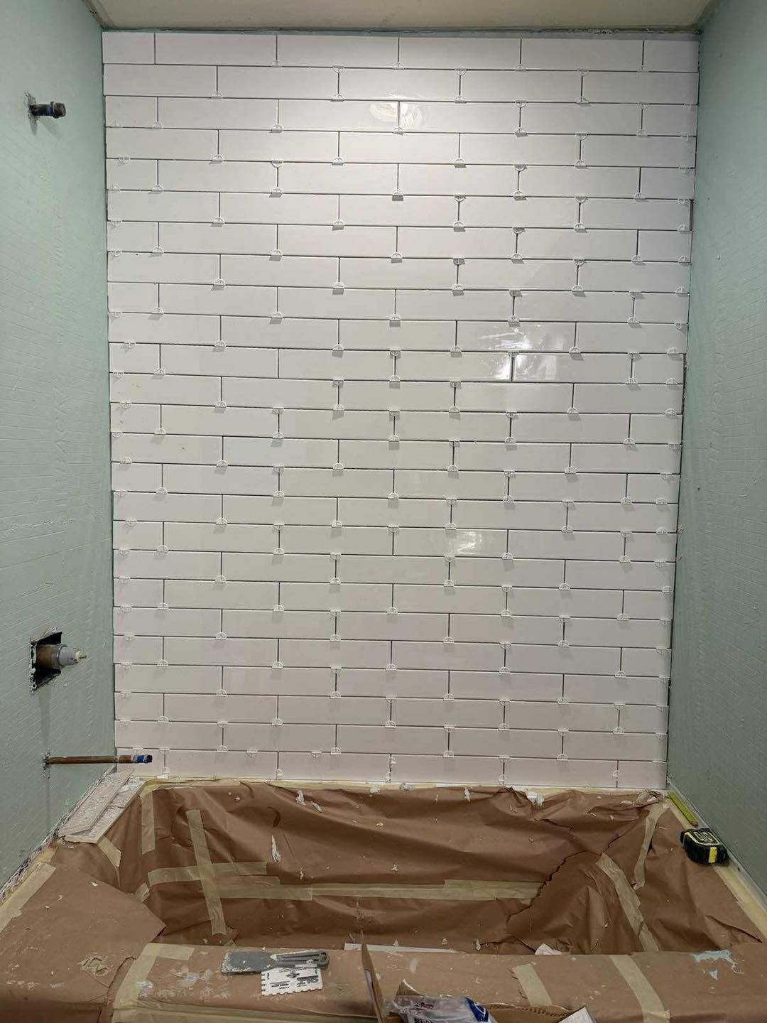 White tilework in progress on a bathroom wall above a bathtub.