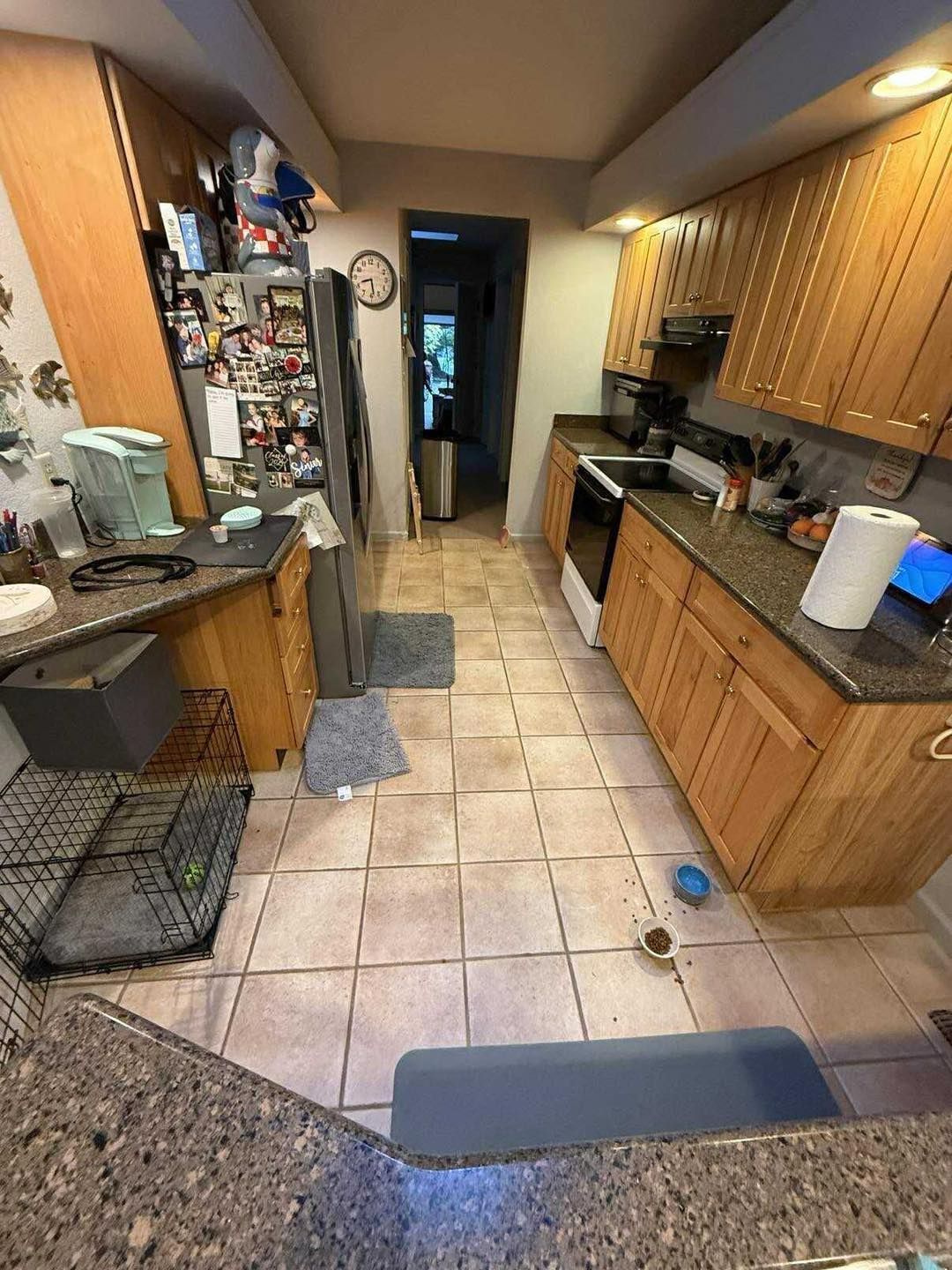 Kitchen with light wood cabinets, dark countertops, and tiled floor. A refrigerator, stove, and dog crate are visible.