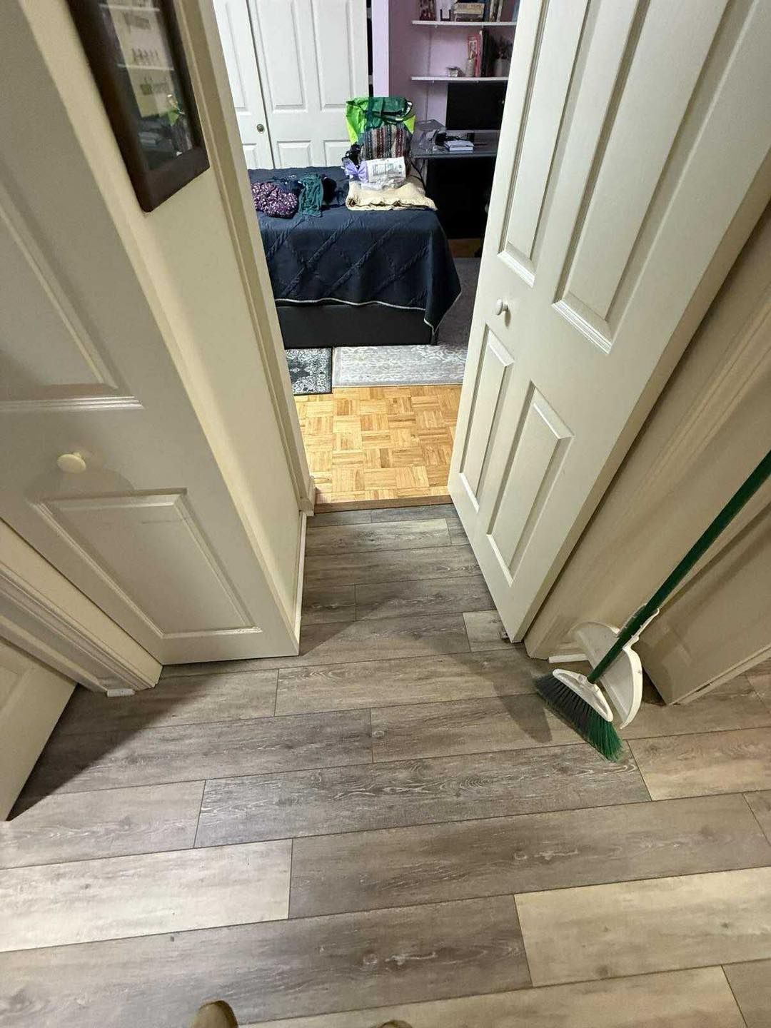 Open doors to a bedroom with bed, desk, and hardwood floor. Broom leaned against the right door.