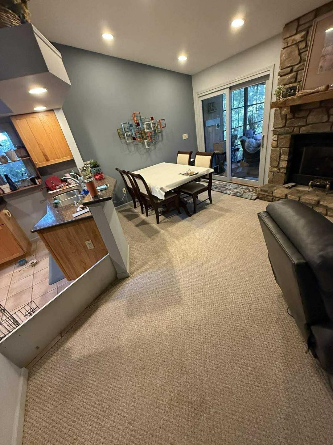 A dining room with a table, chairs, and art on a blue wall. Beige carpet, fireplace, and sliding door.