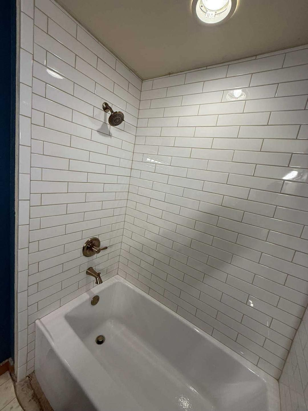 White-tiled shower with tub, bronze fixtures, and overhead light in a bathroom.