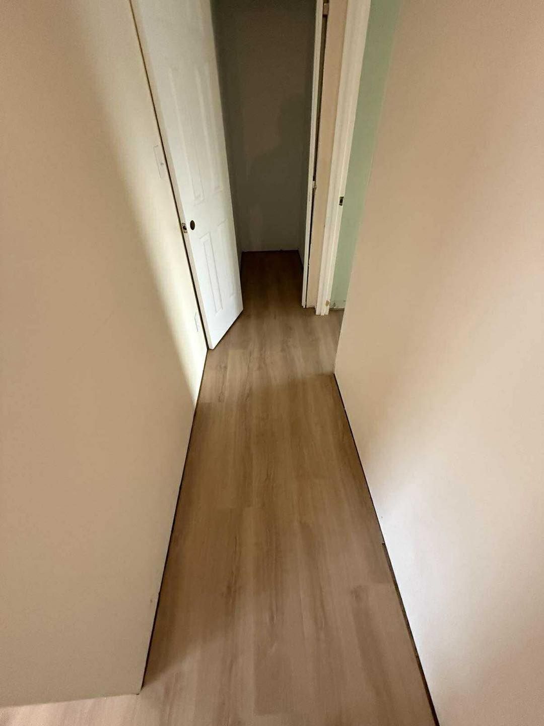 Narrow hallway with wood-look flooring and two doorways, one open.