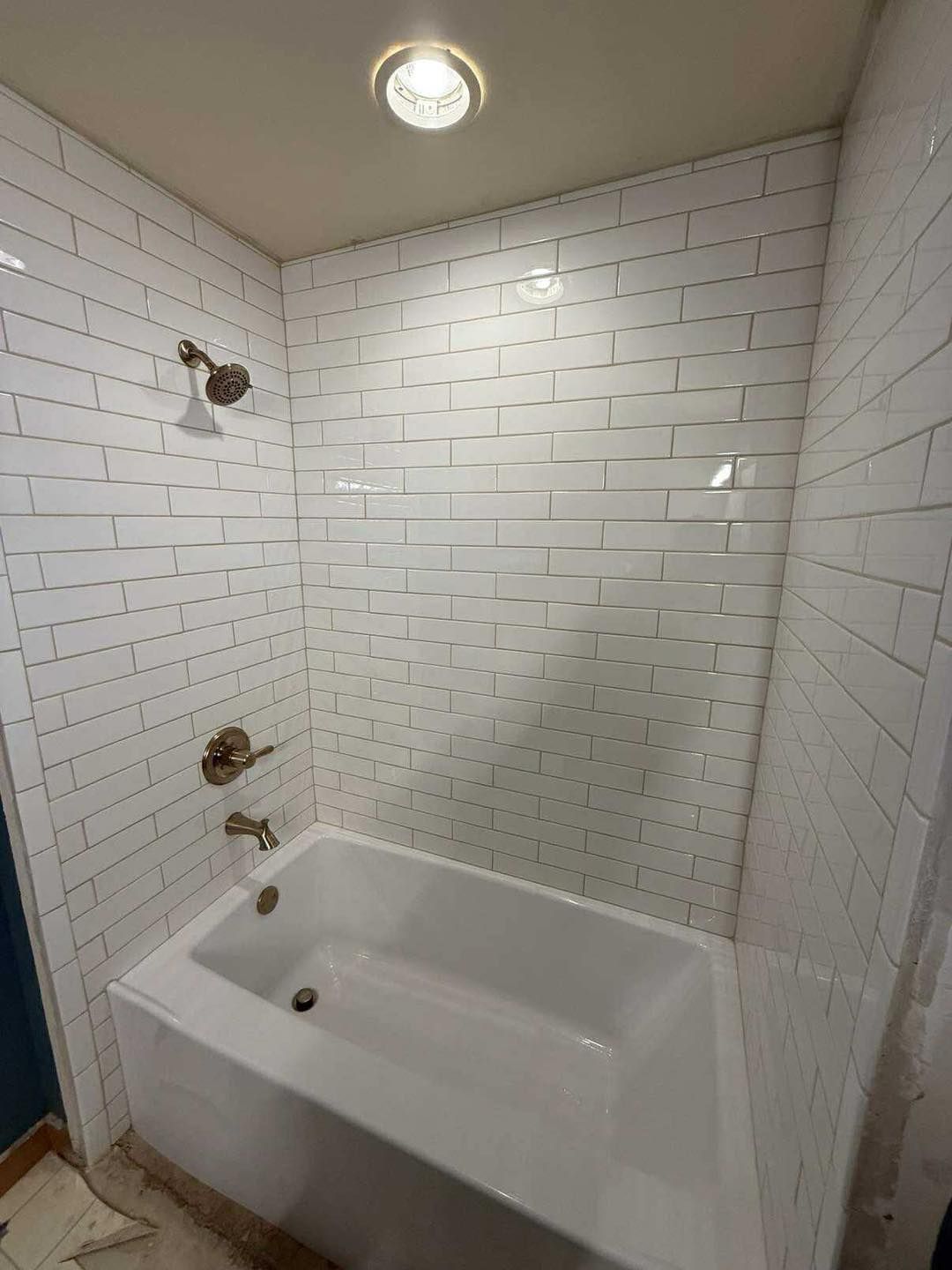 White tiled shower enclosure with bathtub, showerhead, and faucet.
