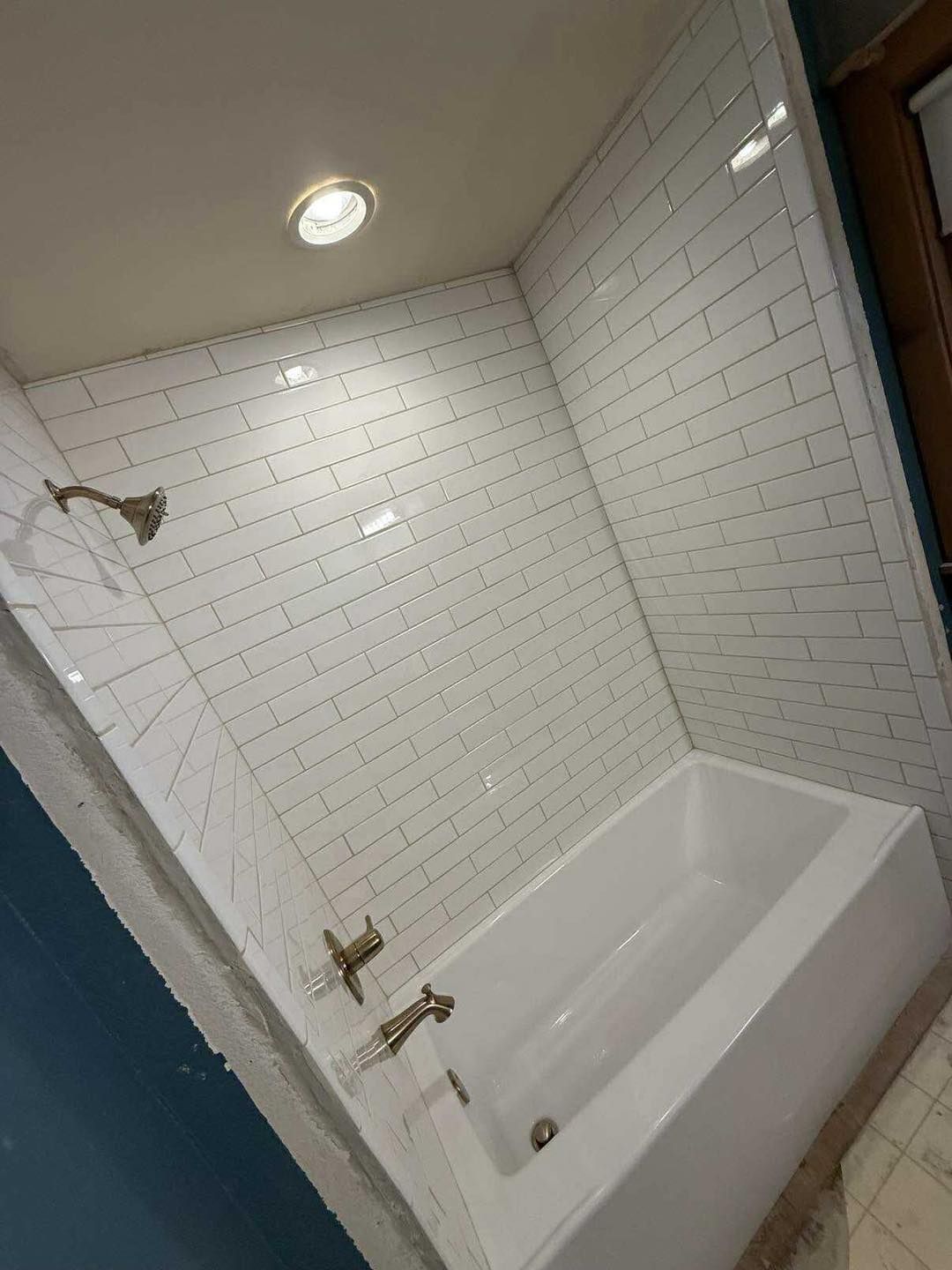 White-tiled shower with gold fixtures and a white bathtub. Recessed lighting.
