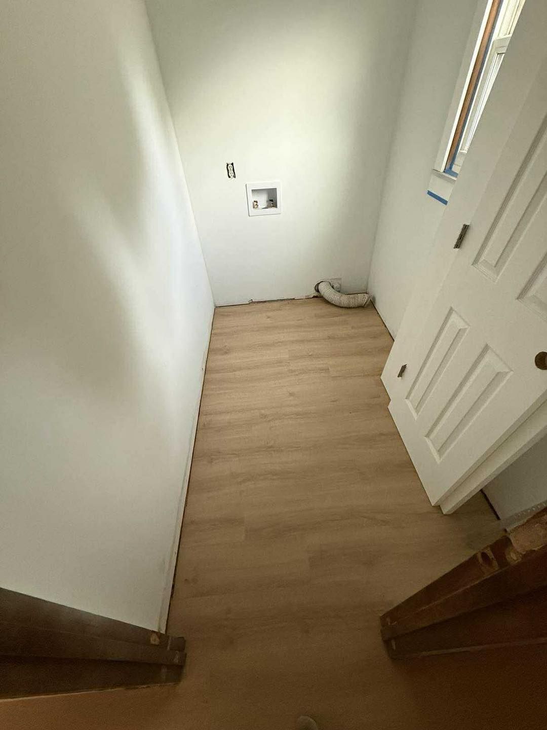 Small, narrow room with wood-look flooring, white walls, laundry hookup, and a door, likely a utility closet.