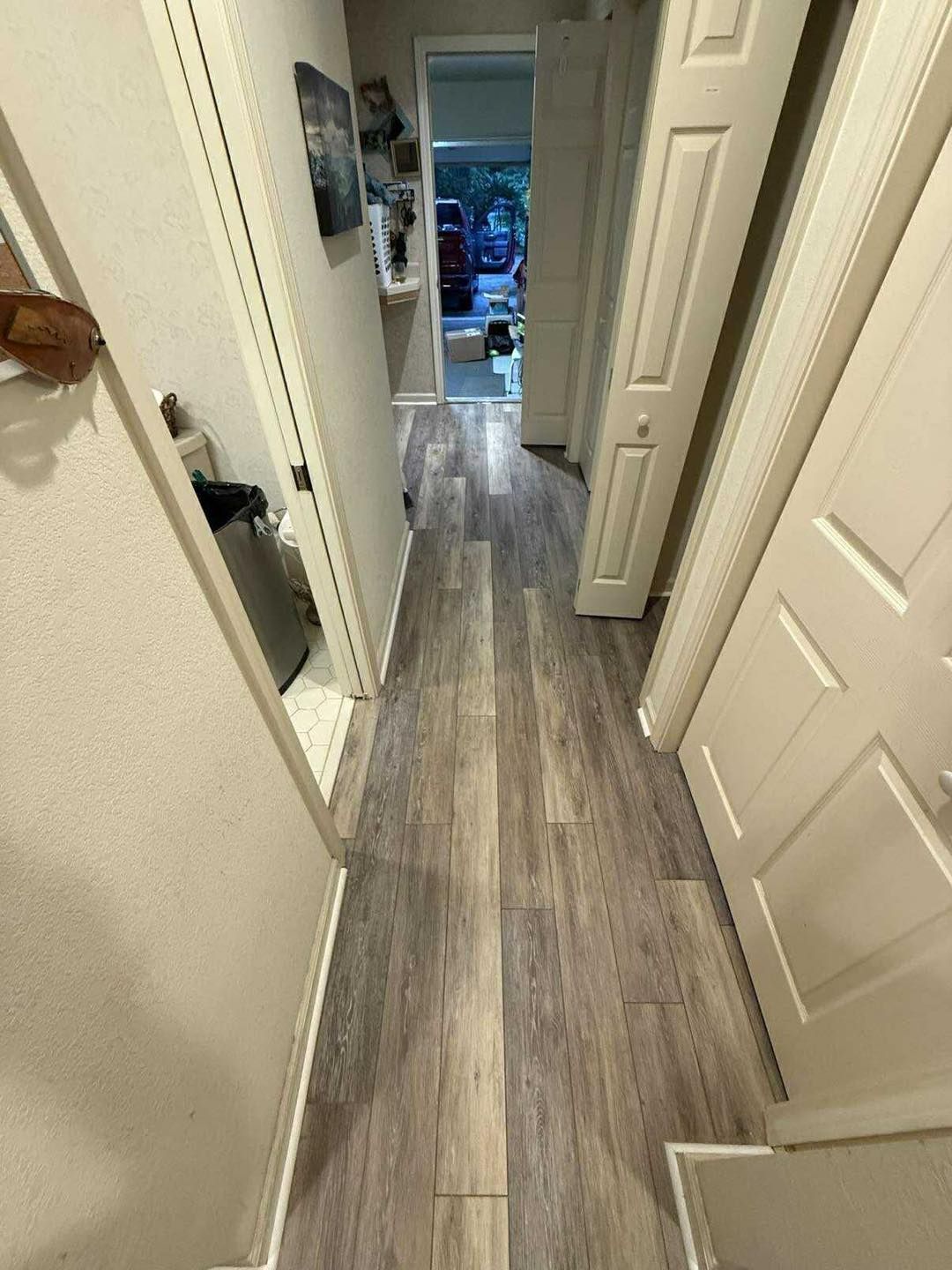 Narrow hallway with light wood-look flooring and cream-colored walls, leading to an open doorway at the end.