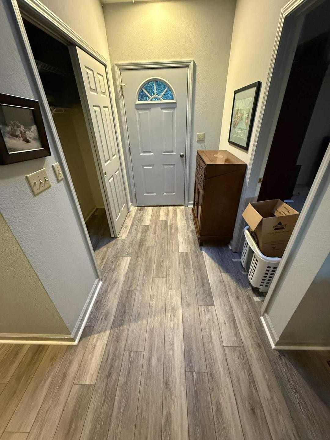 Entryway with wood-look flooring, white door with glass, closet door, wooden cabinet, and artwork.