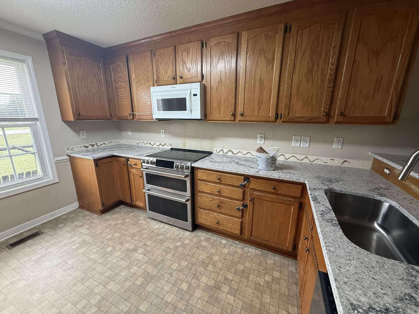 Kitchen with wood cabinets, white countertops, a stove, microwave, and a window.