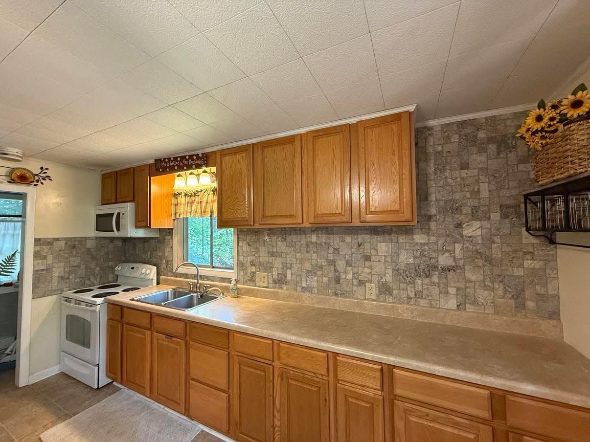 Kitchen with wooden cabinets, beige countertops, and gray backsplash. Appliances include a stove and microwave.