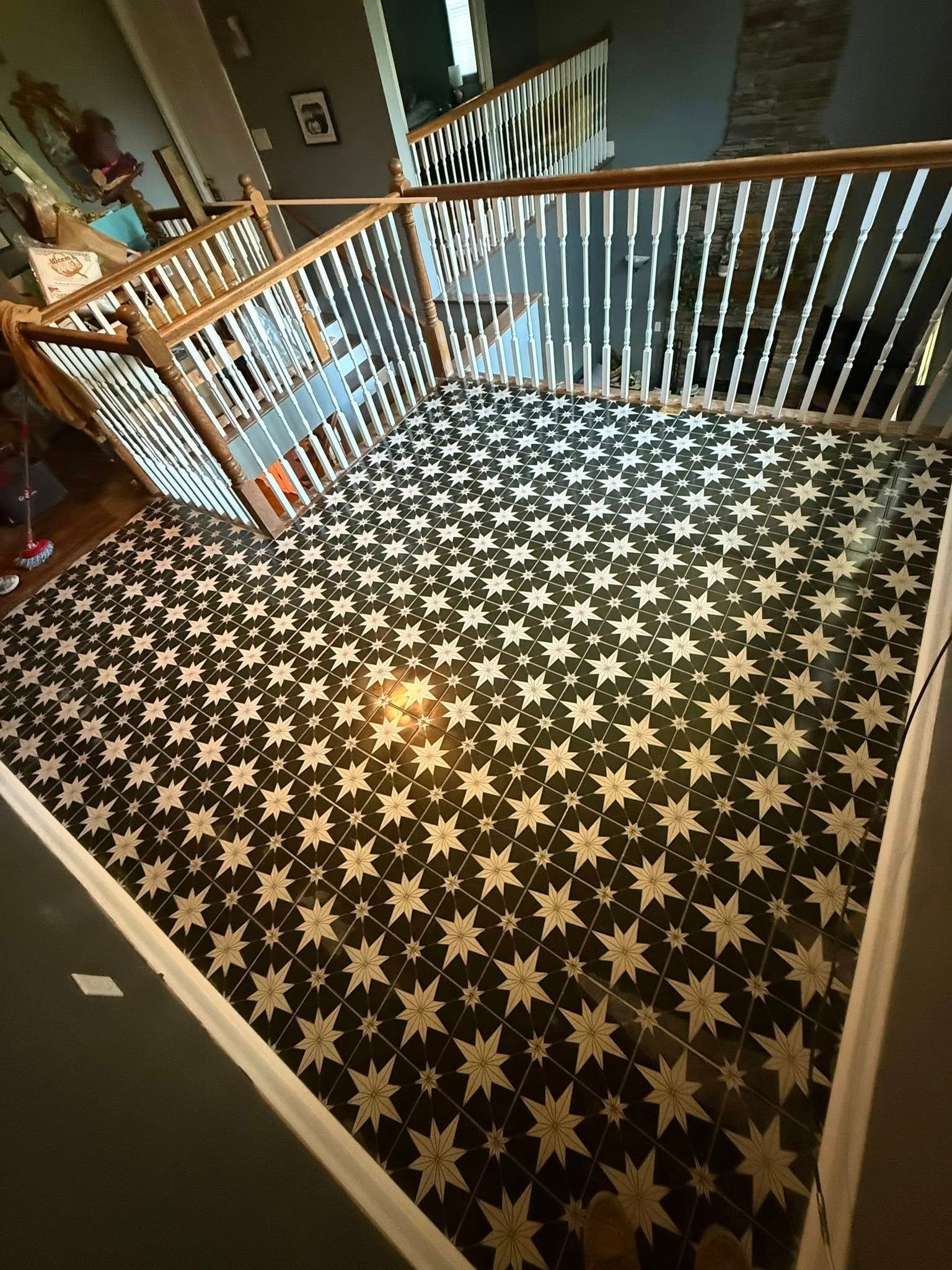 Black and white patterned tile flooring in a hallway with a staircase and white railing.