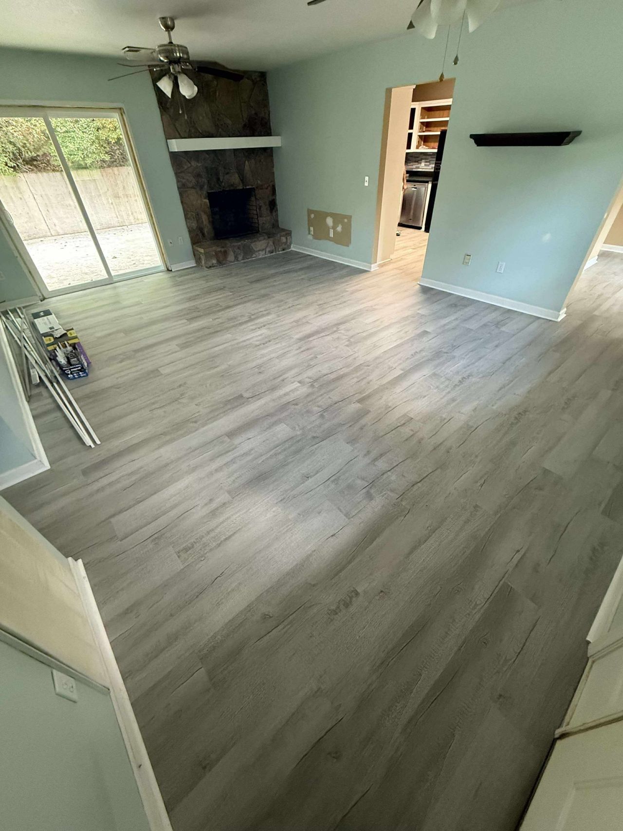 Newly installed gray wood-look flooring in a living room with a fireplace, a sliding glass door, and light blue walls.