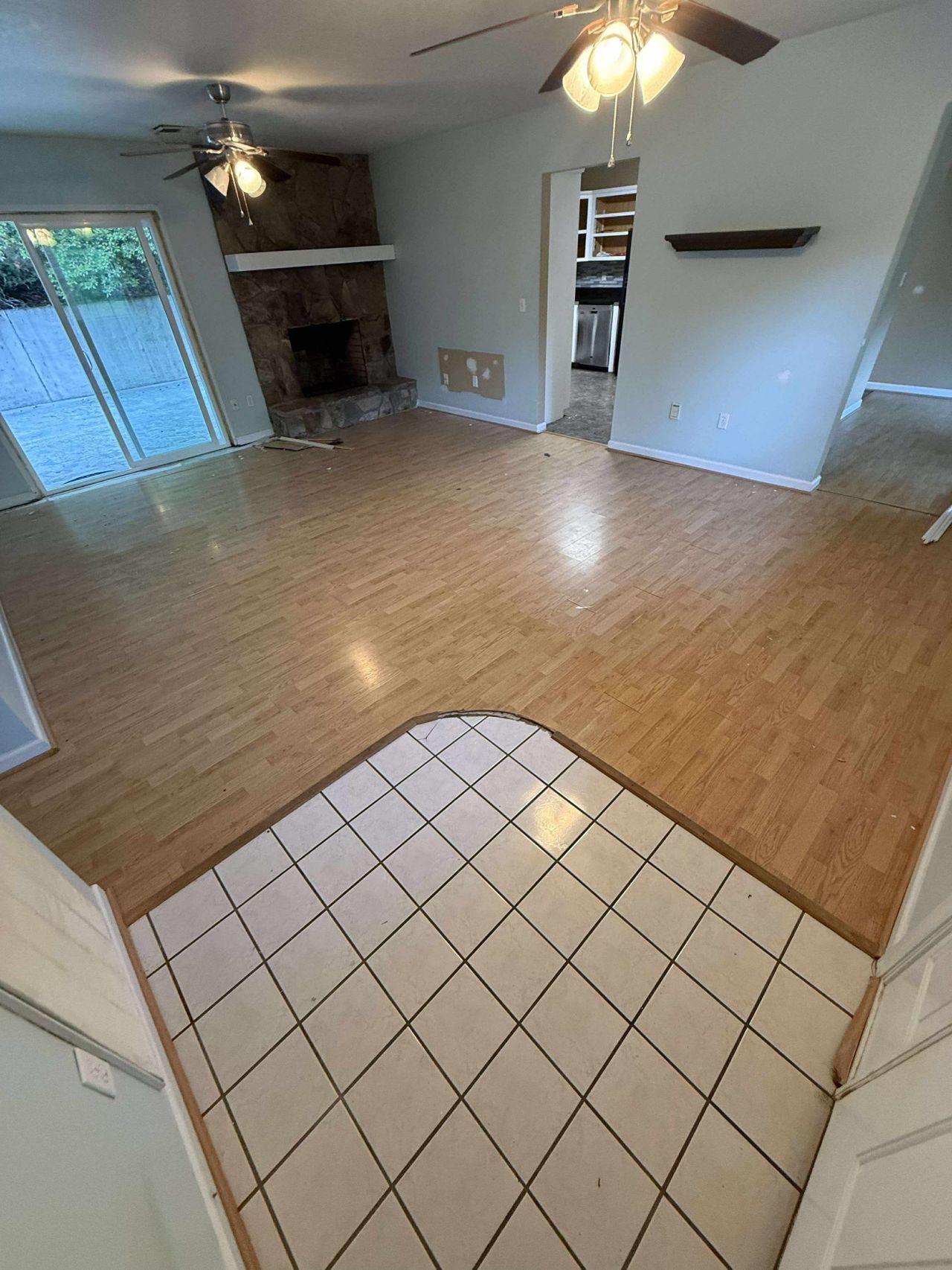 Interior view of a living room with tile floor entryway and wood flooring. Fireplace and sliding glass door are visible.