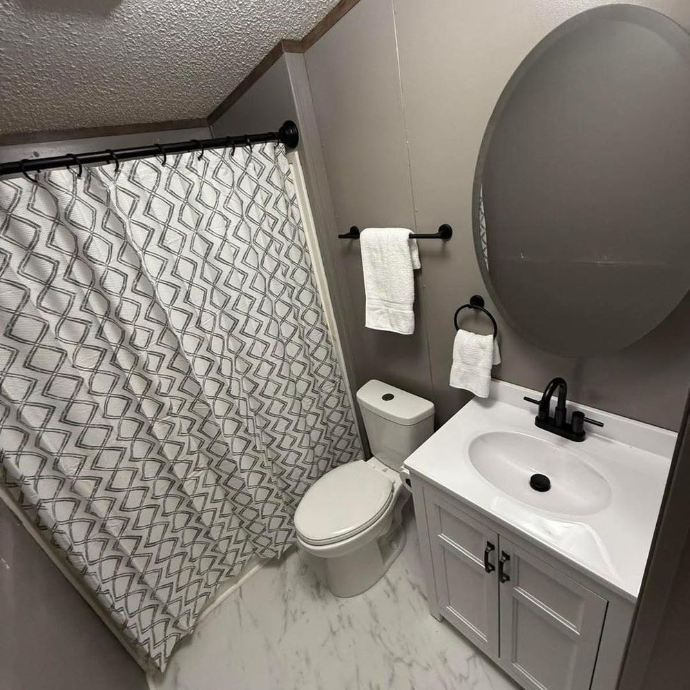 Small bathroom with white vanity, toilet, and shower with patterned curtain.