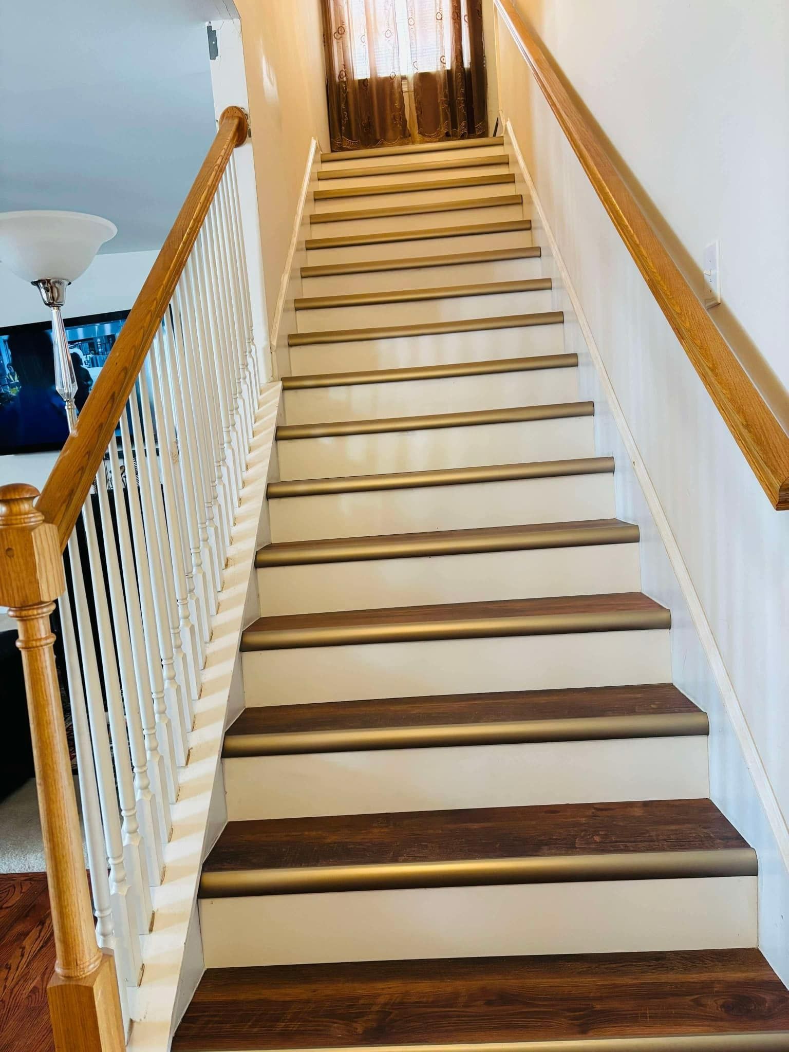 Staircase with brown treads, beige risers, and white banister, leading upwards toward a window.