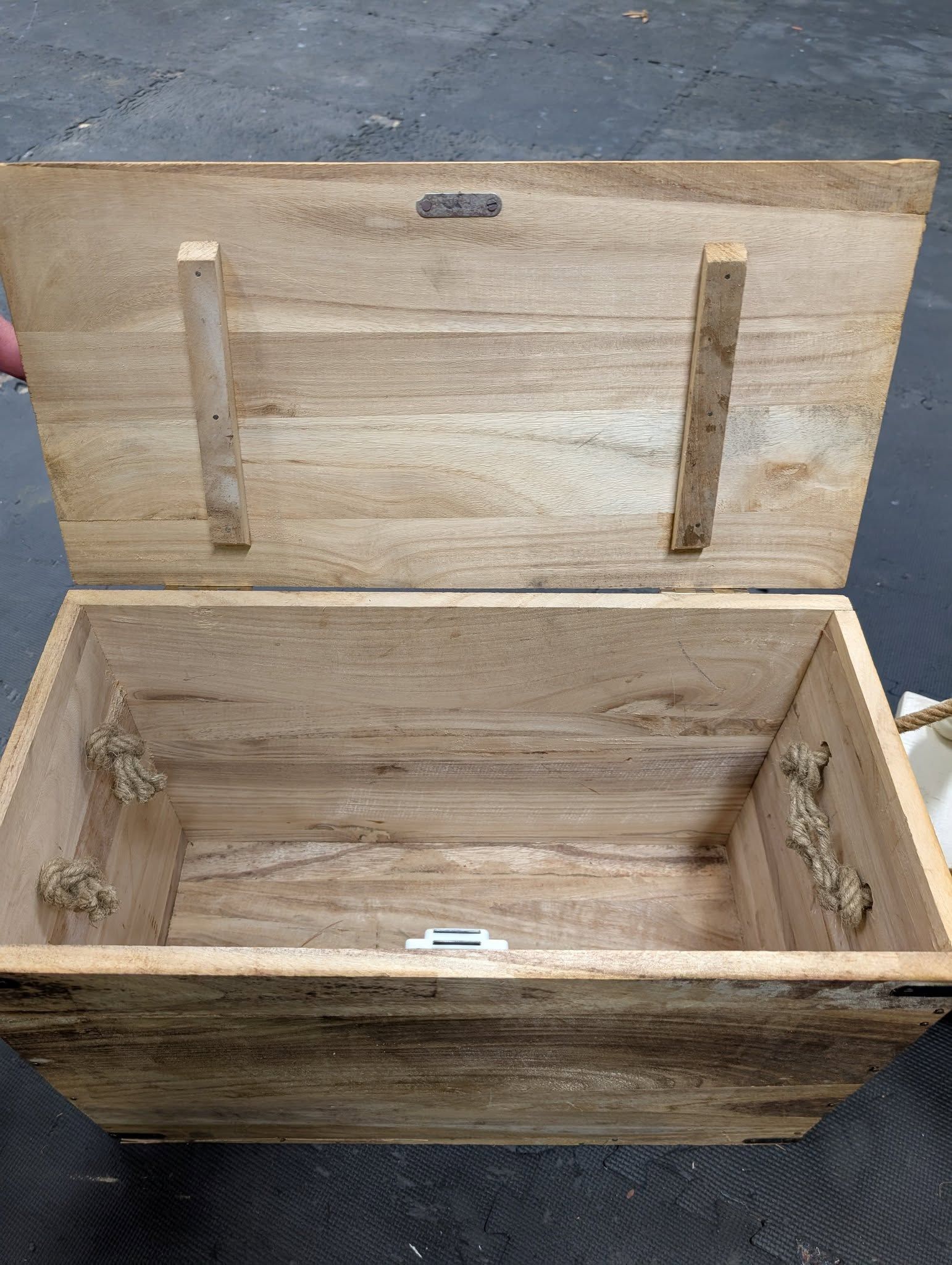 Open wooden chest with a hinged lid. Rope handles on sides, wooden dowels for lid support.