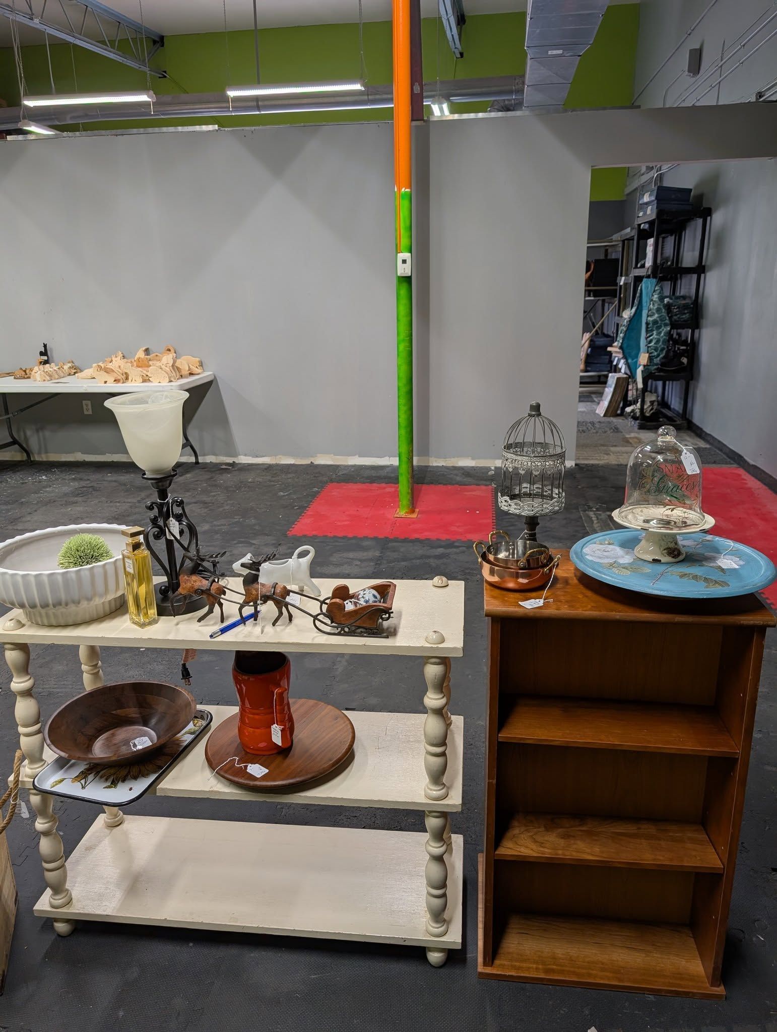 Shelves display various items in a room. A tall pole stands between the shelves and a table.